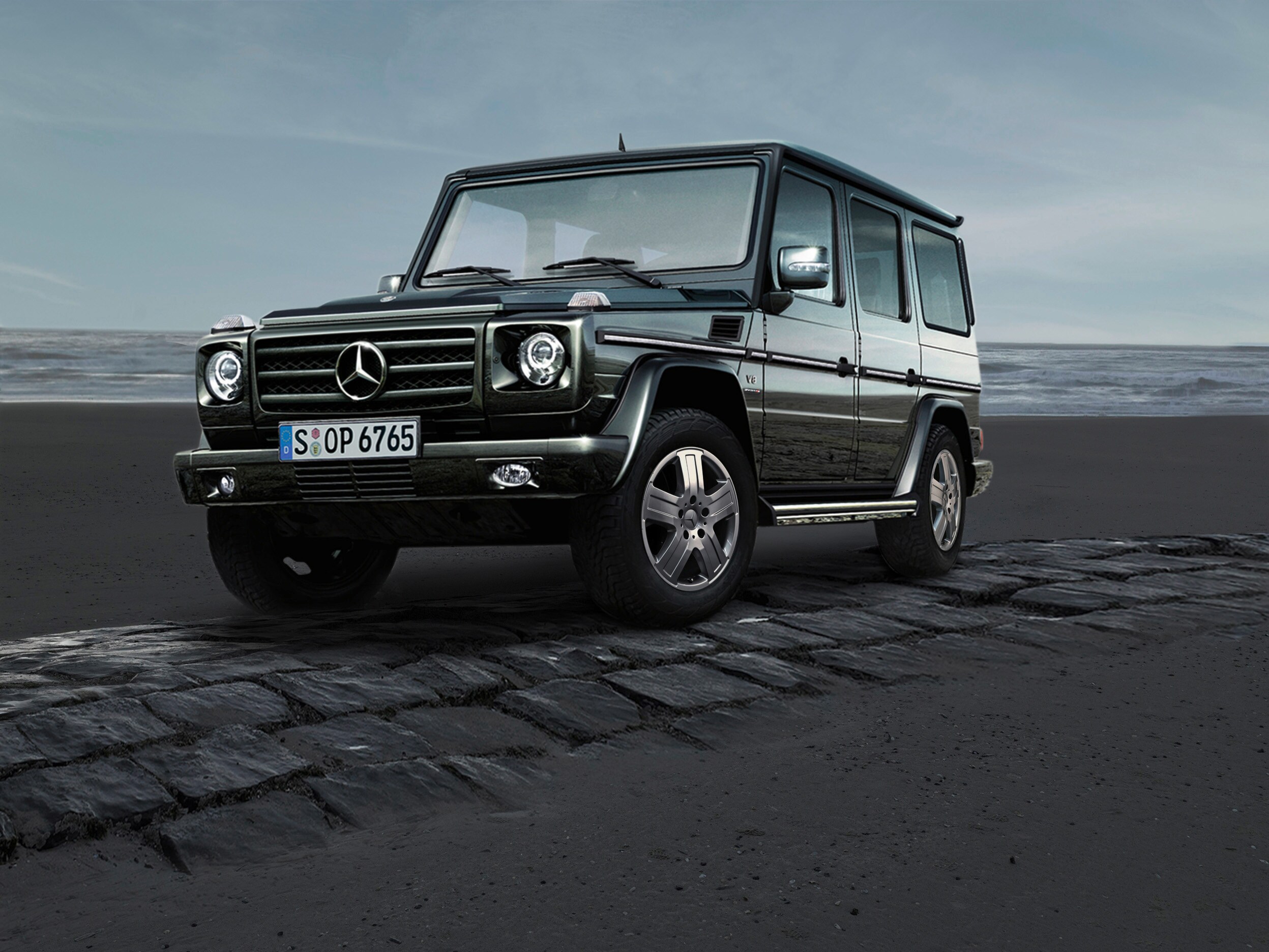 Eine dunkle G-Klasse von Mercedes-Benz steht auf einem gepflasterten Streifen vor der Küste.
