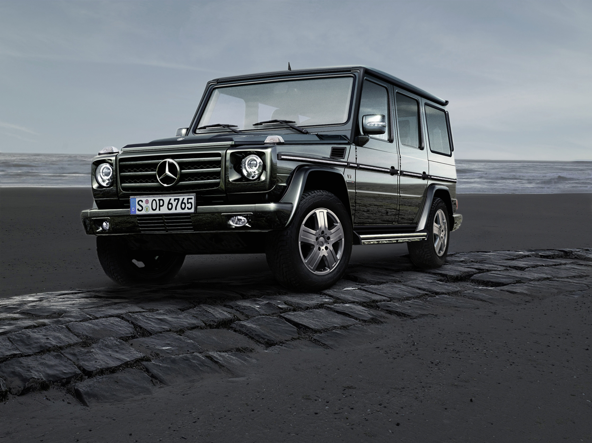 Service- und Garantiepakete | Mercedes-Benz. Eine dunkle G-Klasse von Mercedes-Benz steht auf einem gepflasterten Streifen vor der Küste.