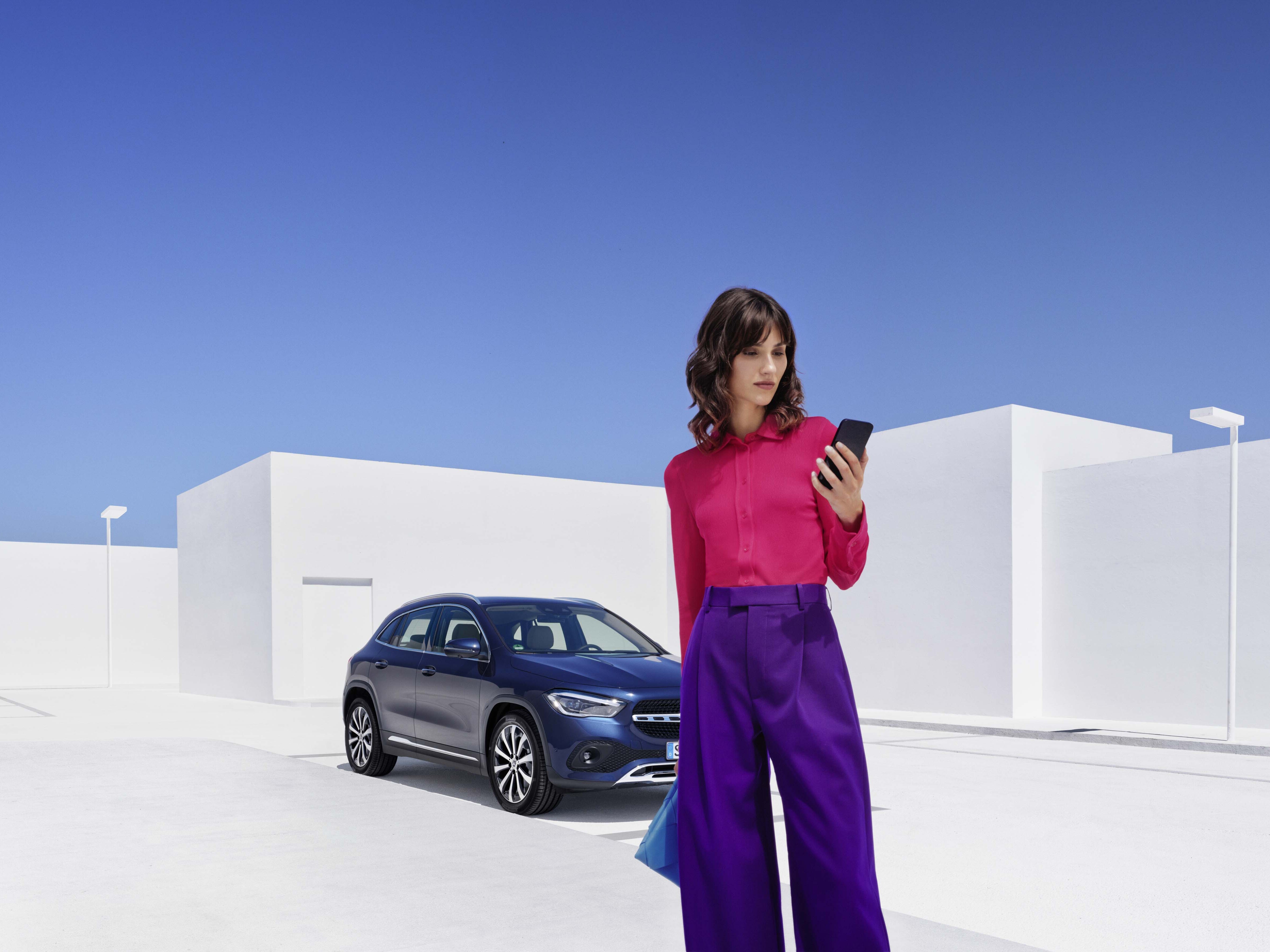 Frau mit Handy in der Hand vor einem Mercedes-Benz.