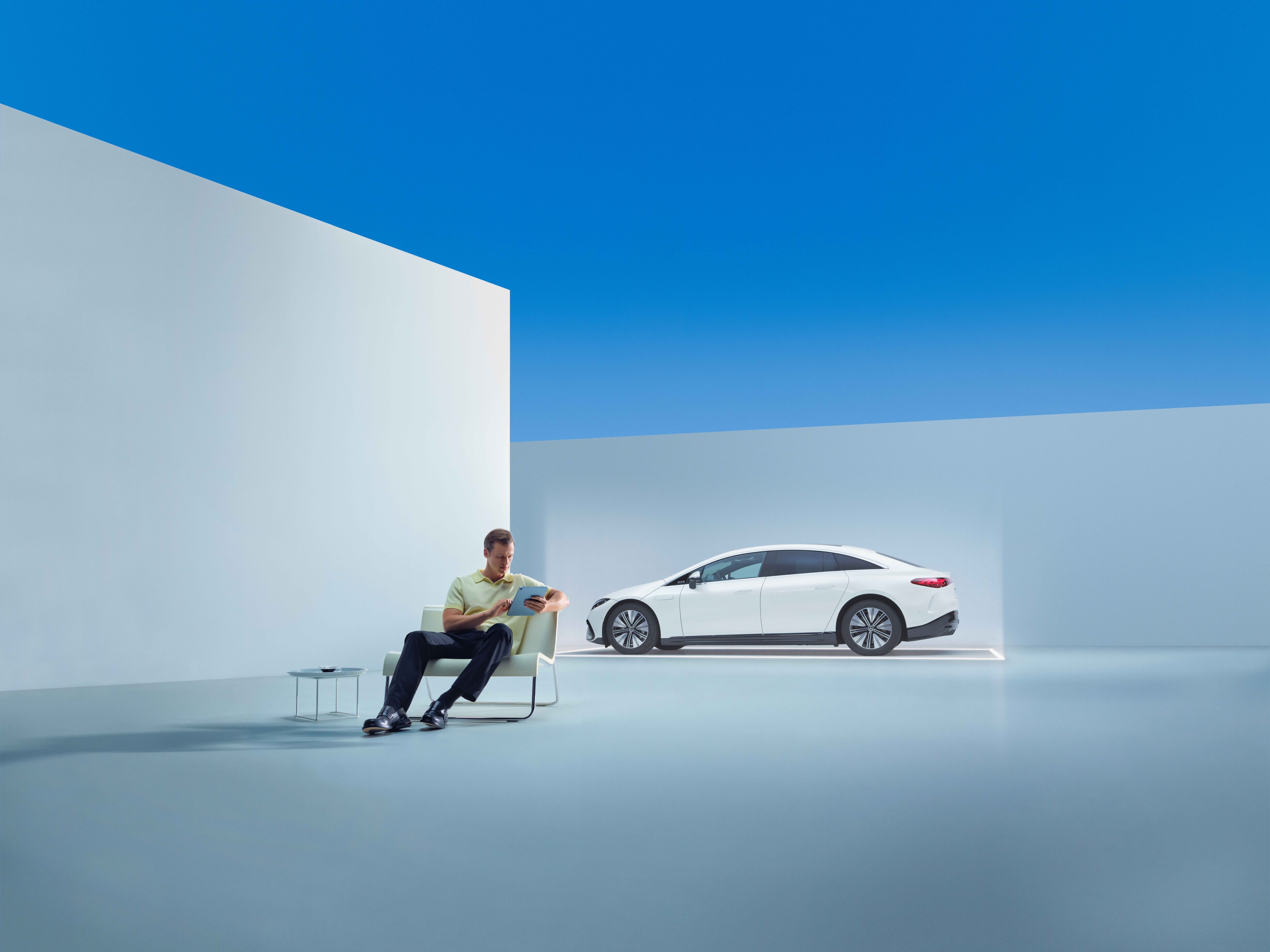 Mann sitzt auf einem Stuhl vor einem weißen Mercedes-Benz