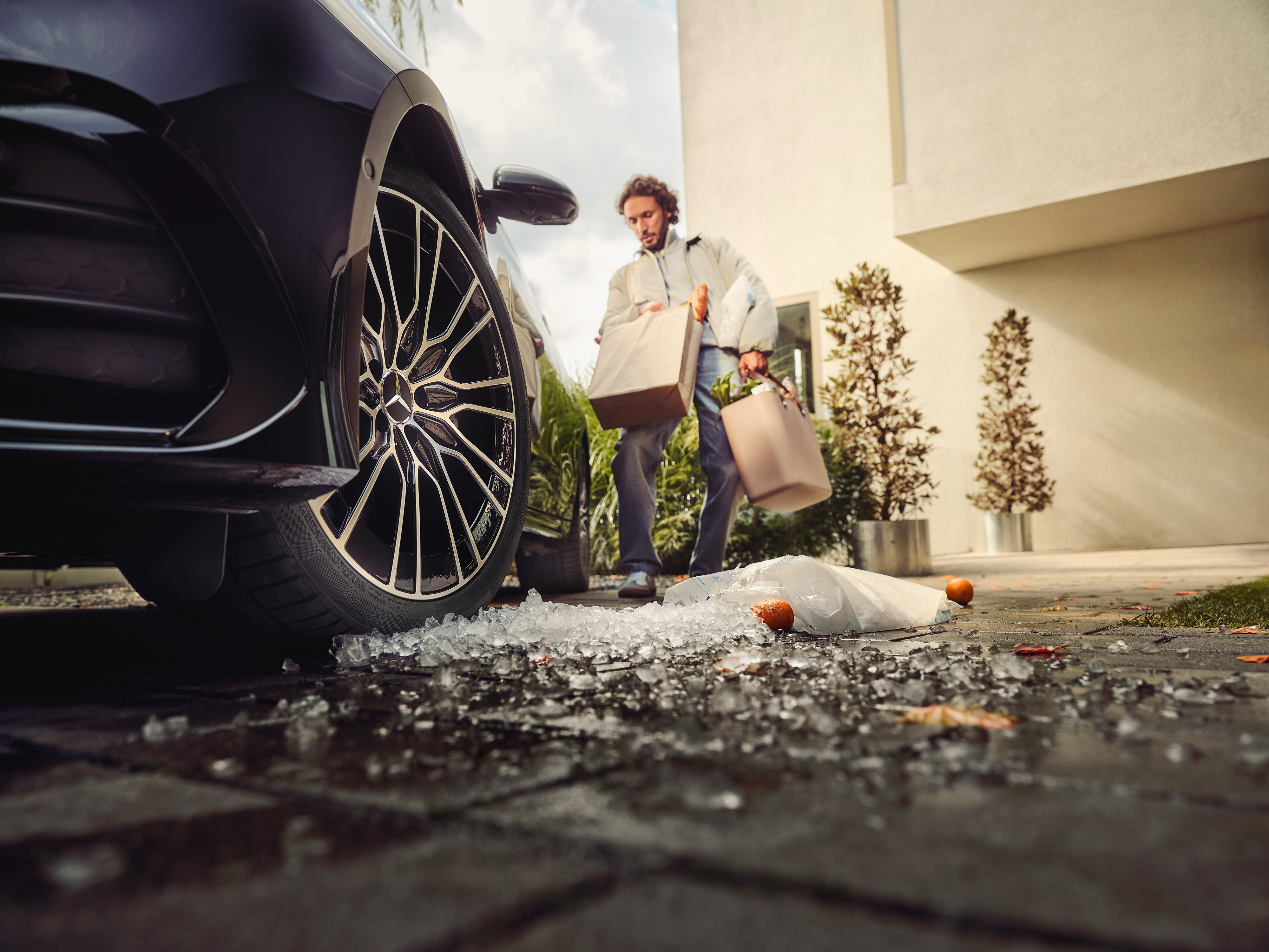 Cashback | Mercedes Benz Ein Mann mit voll beladen mit Einkaufstüten geht zu seinem Mercedes-Benz, wobei einige Sachen schon auf dem Boden liegen.