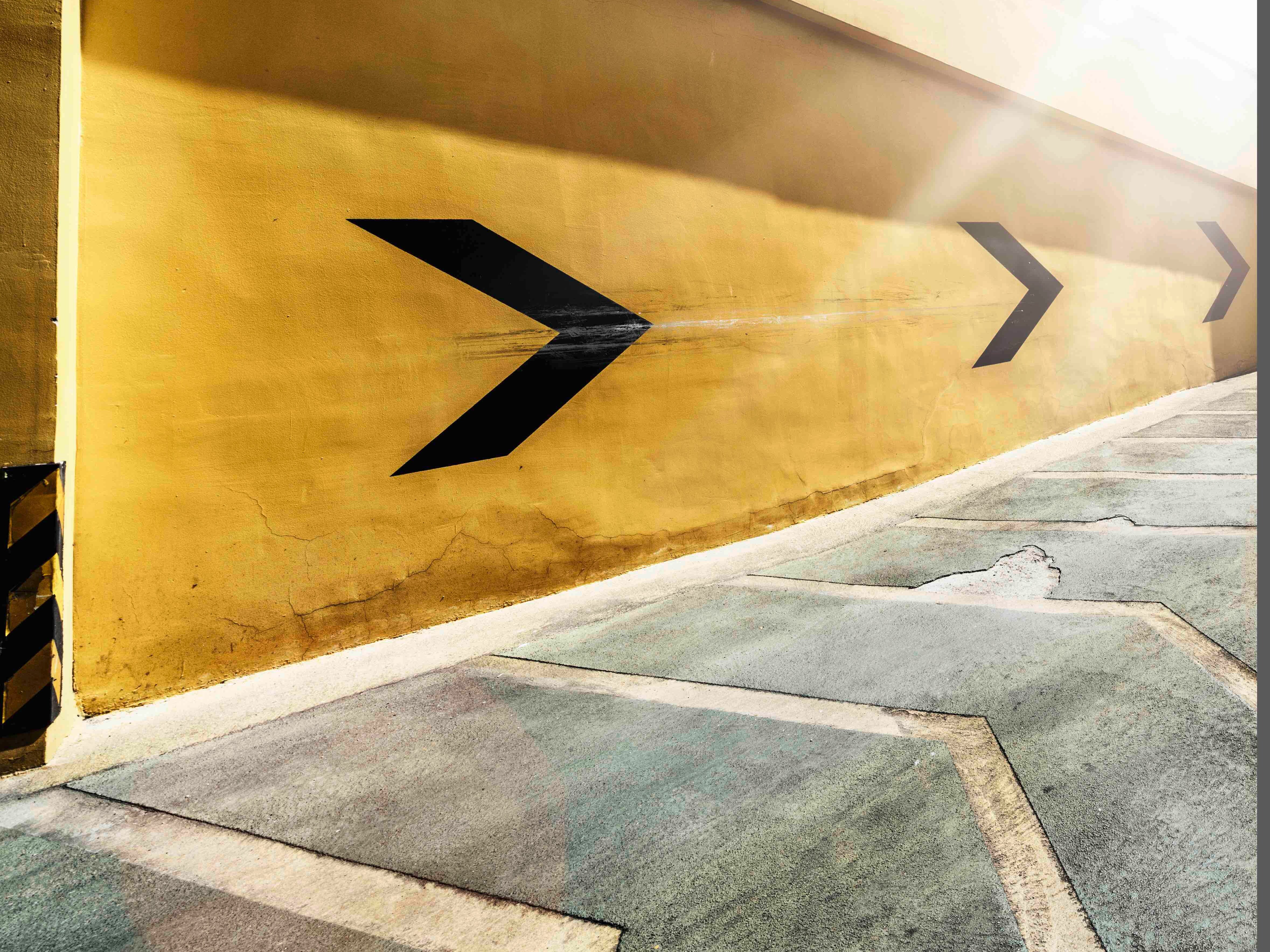 Eine gelbe Wand mit schwarzen Pfeilen und Sonnenschein.