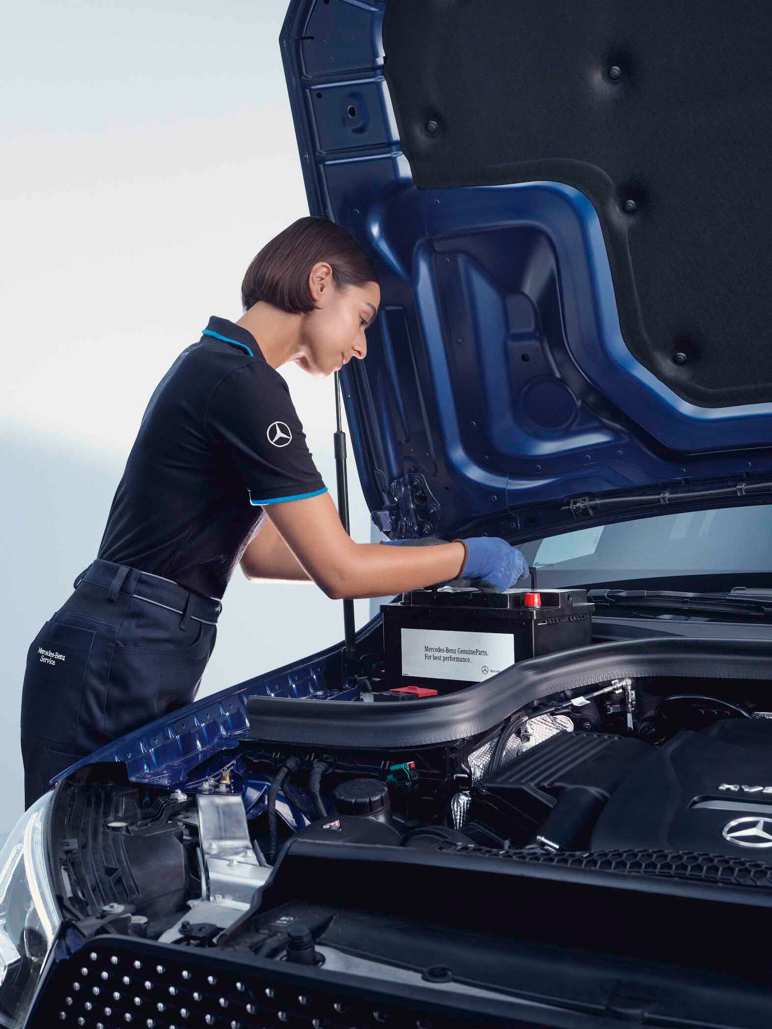 Ein Automechaniker beugt sich über die geöffnete Motorhaube eines Mercedes-Benz.