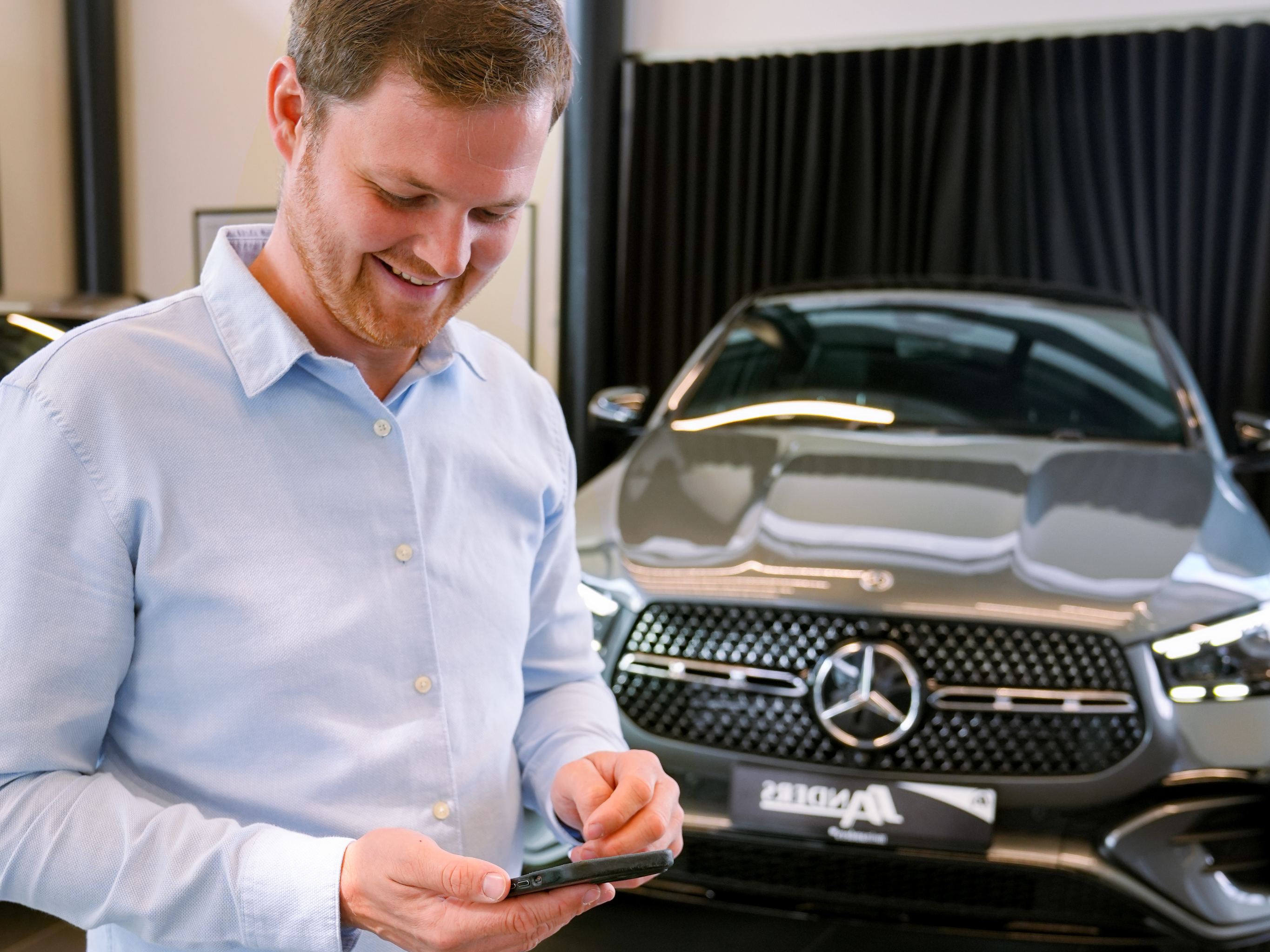 Mercedes-Benz Fahrtenbuch Ein Mann tippt auf seinem Handy und lächelt.