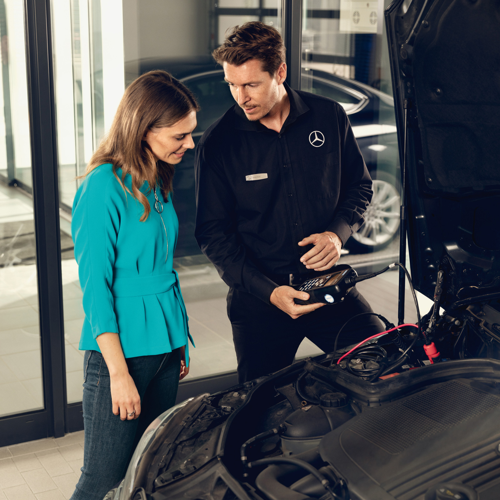 Herbstaktion | Mercedes-Benz Ein Mann steht neben einer Frau mit einem Gerät zur Analyse der Batteriefunktion.
