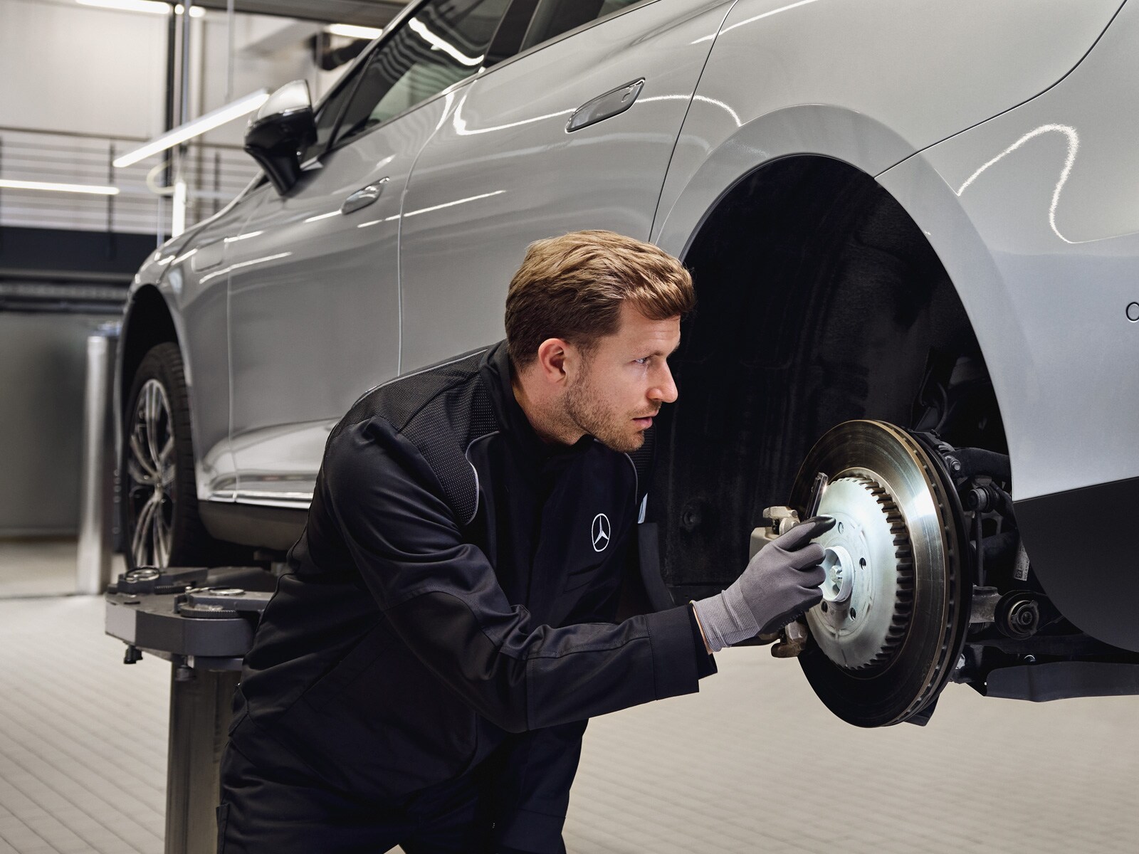 Ein Mann arbeitet an den Bremsen eines silbernen Mercedes-Benz, der auf einer Hebebühne steht.