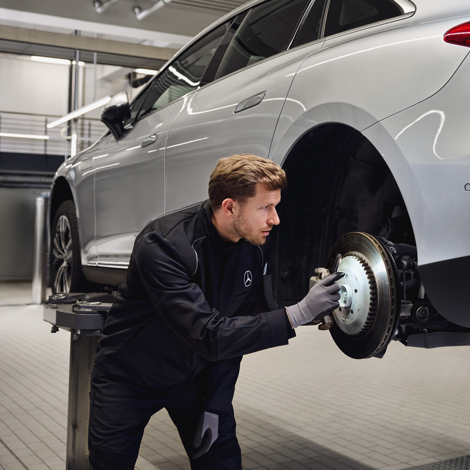 Herbstaktion | Mercedes-Benz Ein Mann arbeitet an den Bremsen eines silbernen Mercedes-Benz, der auf einer Hebebühne steht.