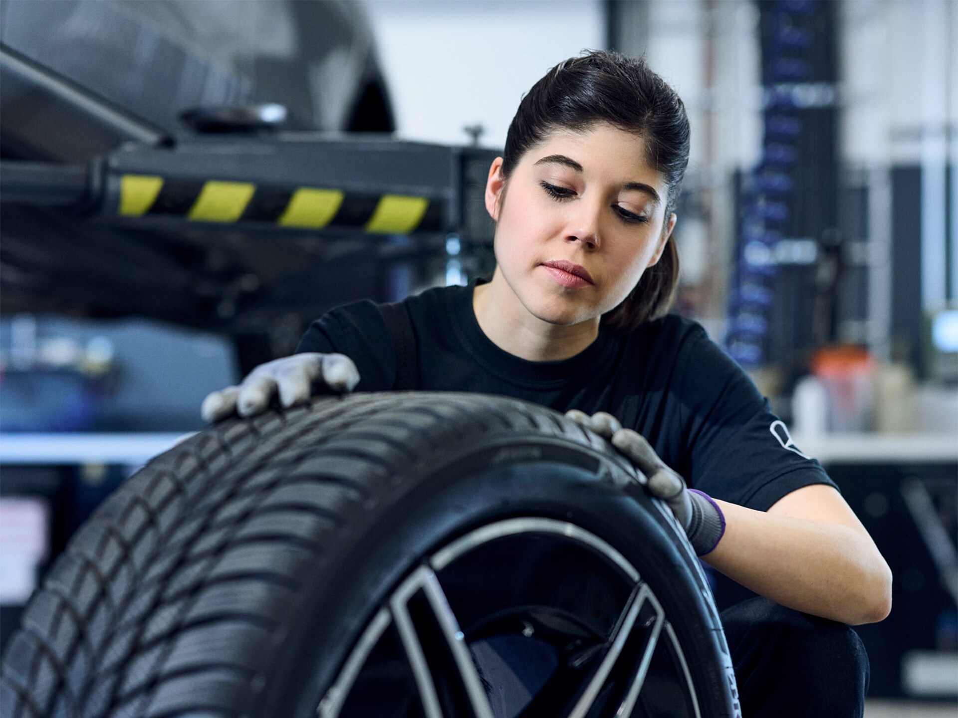 Mercedes-Benz Mechanikerin mit Handschuhen an beim Prüfen der Reifenprofiltiefe.