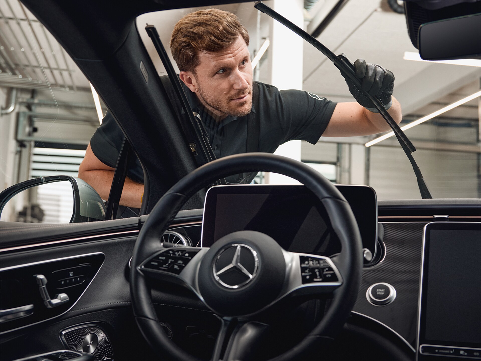 Ein Mercedes-Benz Mechaniker in Arbeitskleidung und Handschuhen beim Ersetzen der Wischblätter.