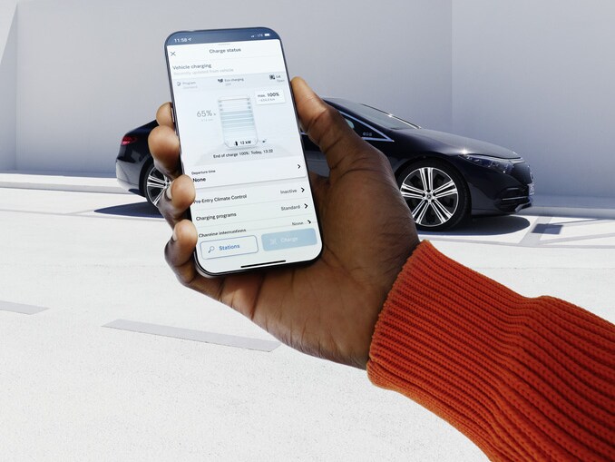 Ein Handy in der Hand einer Person im orangen Pullover, im Hintergrund ist ein Mercedes-Benz