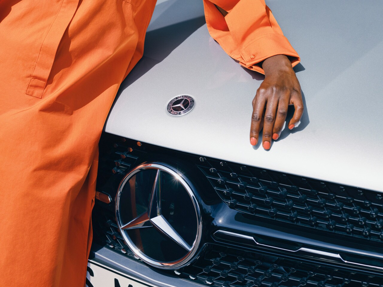 eine Person in einem orangenen Outfit lehnt sich auf einen weißen Mercedes-Benz.