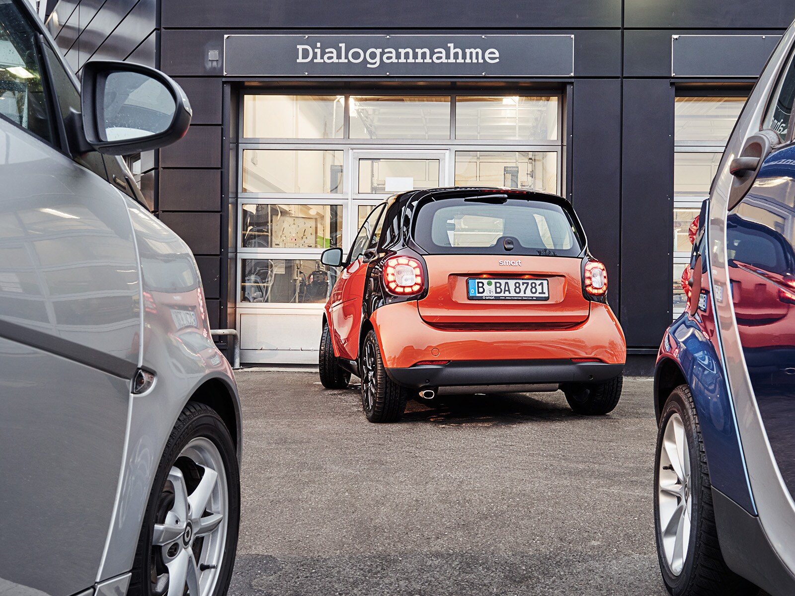 ein orangener Smart vor einer Mercedes-Benz Dialogannahme