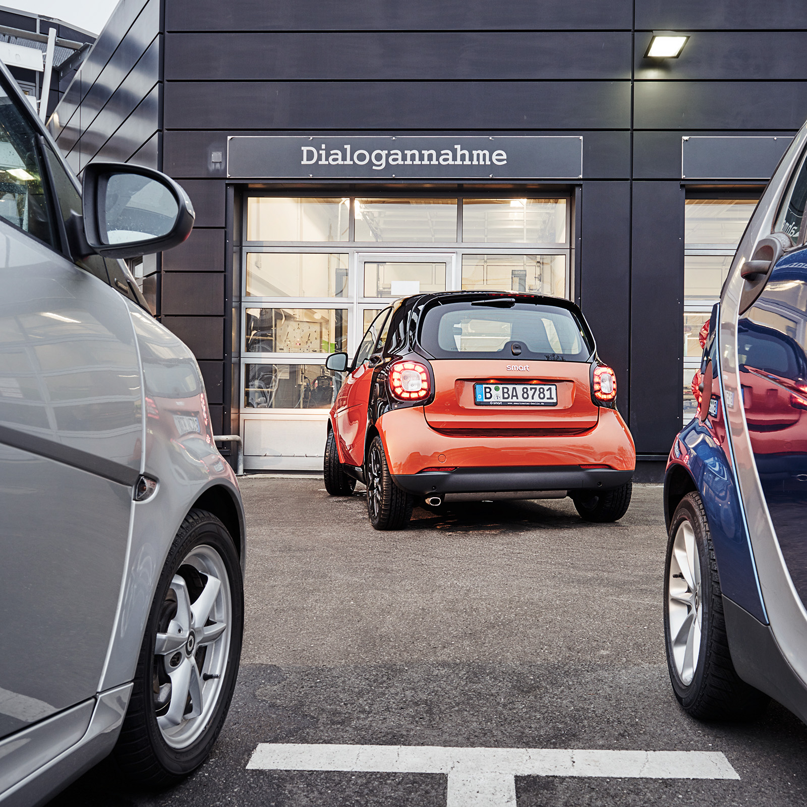 Service | smart ein orangener Smart vor einer Mercedes-Benz Dialogannahme