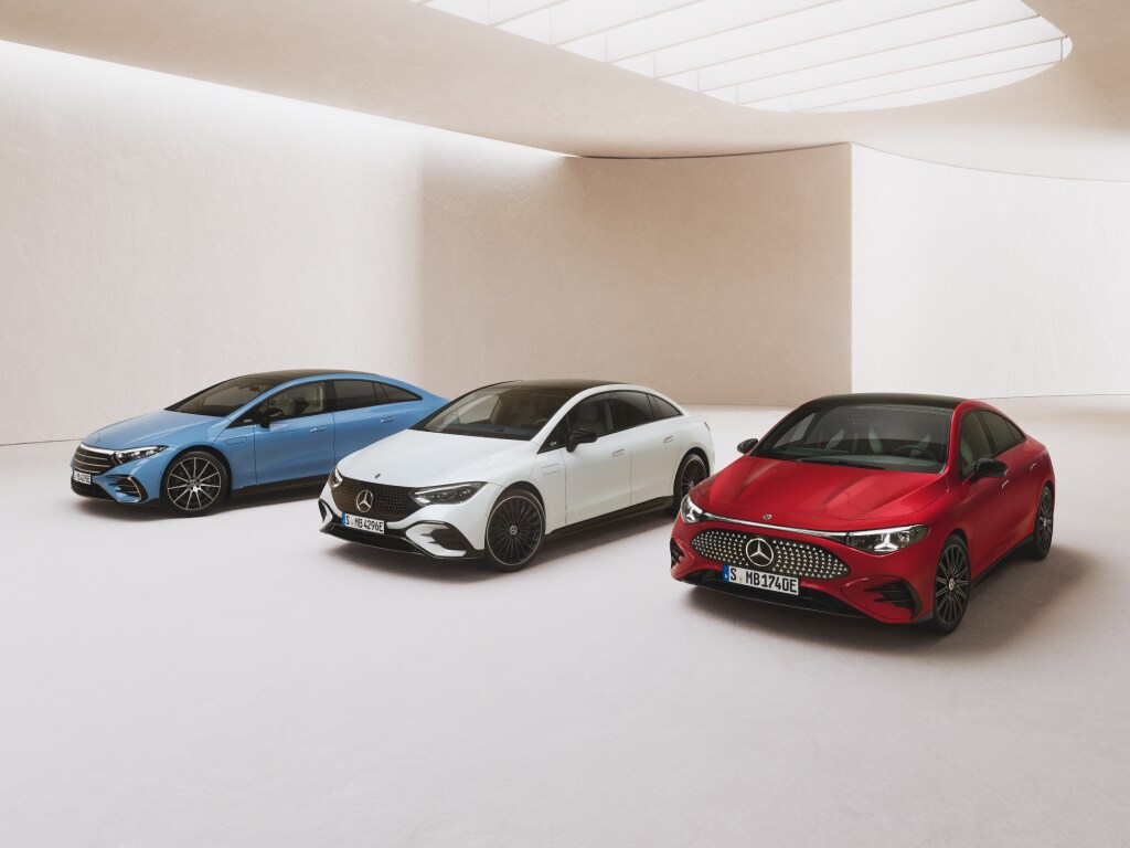 Ein weißer, ein roter und ein blauer vollelektrischer Mercedes-Benz stehen auf hellem Untergrund in einer lichtdurchfluteten Halle.