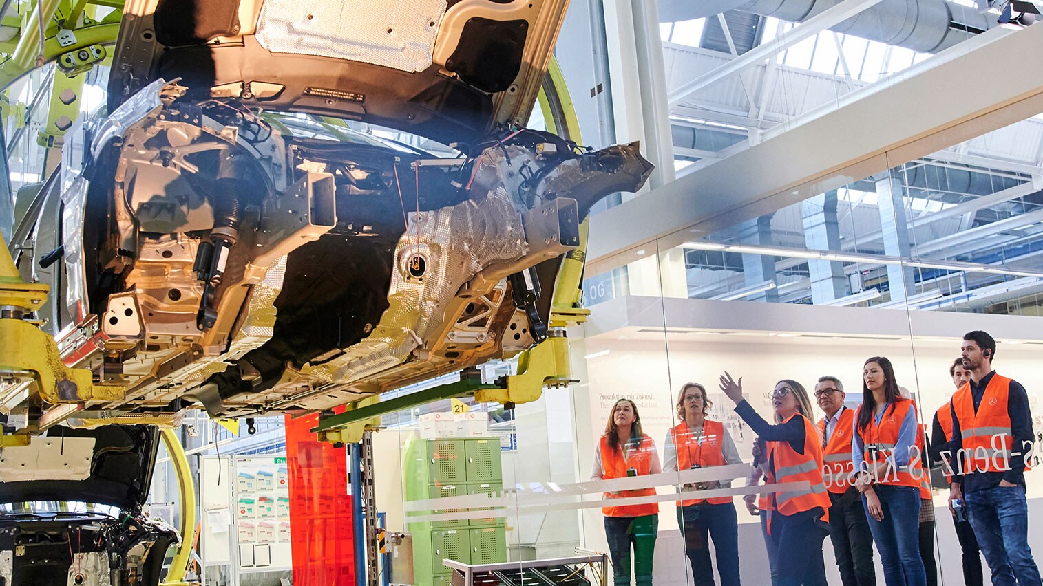 Eine Gruppe von Menschen schaut sich in einer Werkbesichtigung im Kundencenter an, wie ein Mercedes-Benz zusammengebaut wird.