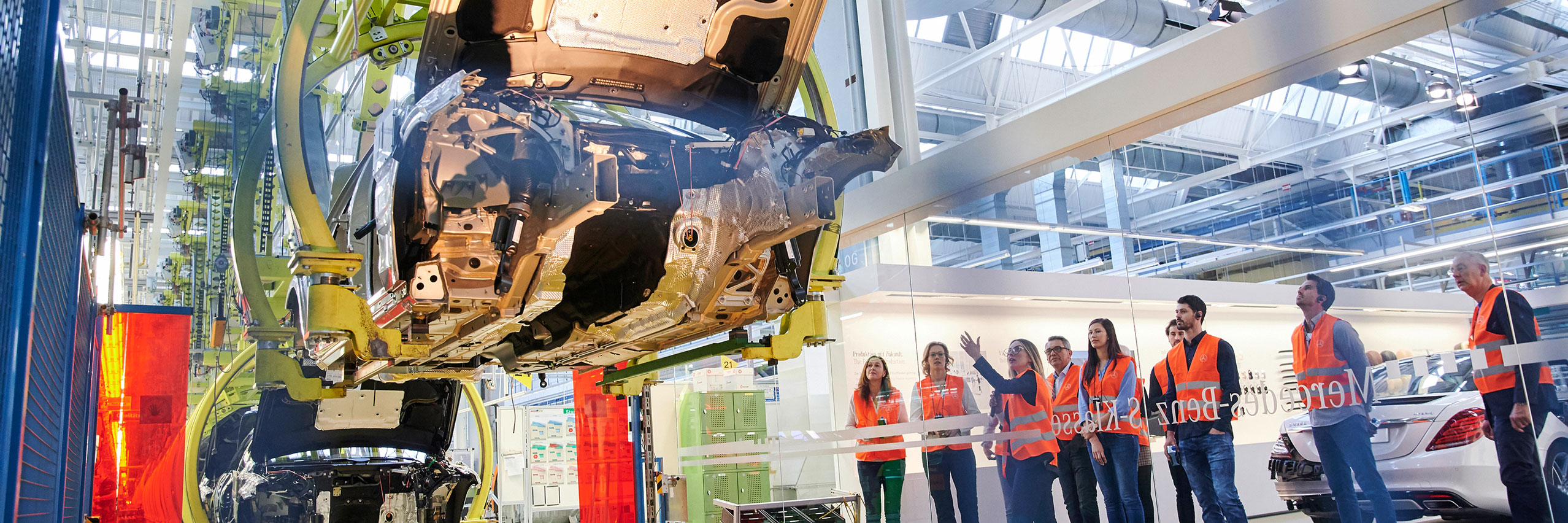 Eine Gruppe von Menschen schaut sich in einer Werkbesichtigung im Kundencenter an, wie ein Mercedes-Benz zusammengebaut wird.