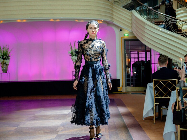 Ein Model in schwarzem Kleid auf einem Laufsteg der Mercedes-Benz Fashion Moments