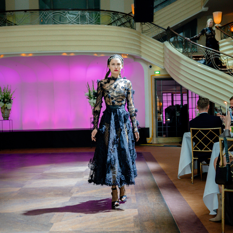 Ein Model auf einem Laufsteg der Mercedes-Benz Fashion Moments Ein Model in schwarzem Kleid auf einem Laufsteg der Mercedes-Benz Fashion Moments