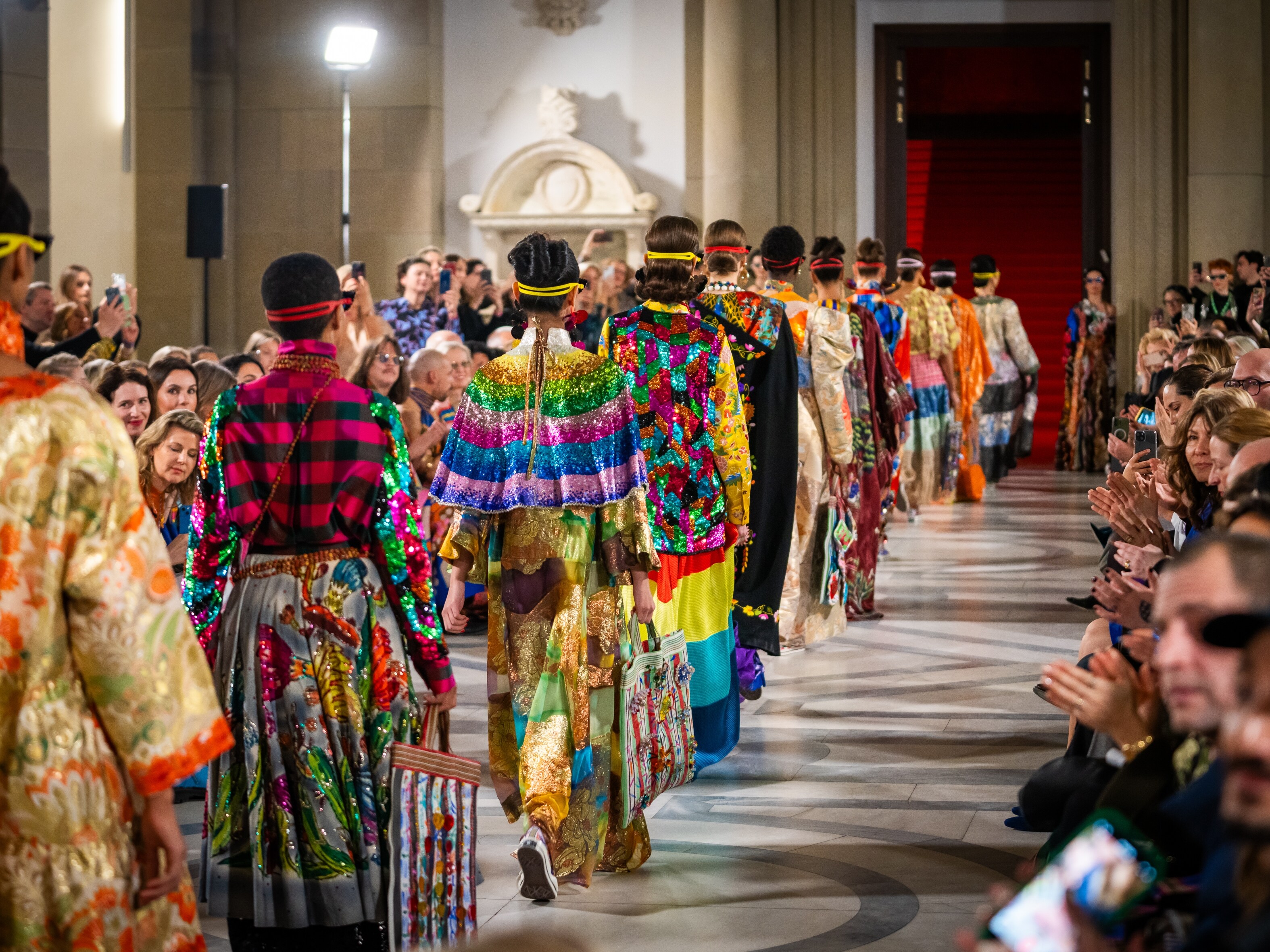 Viele Models auf einem Laufsteg der Mercedes-Benz Fashion Moments in farbenfrohen Outfits.