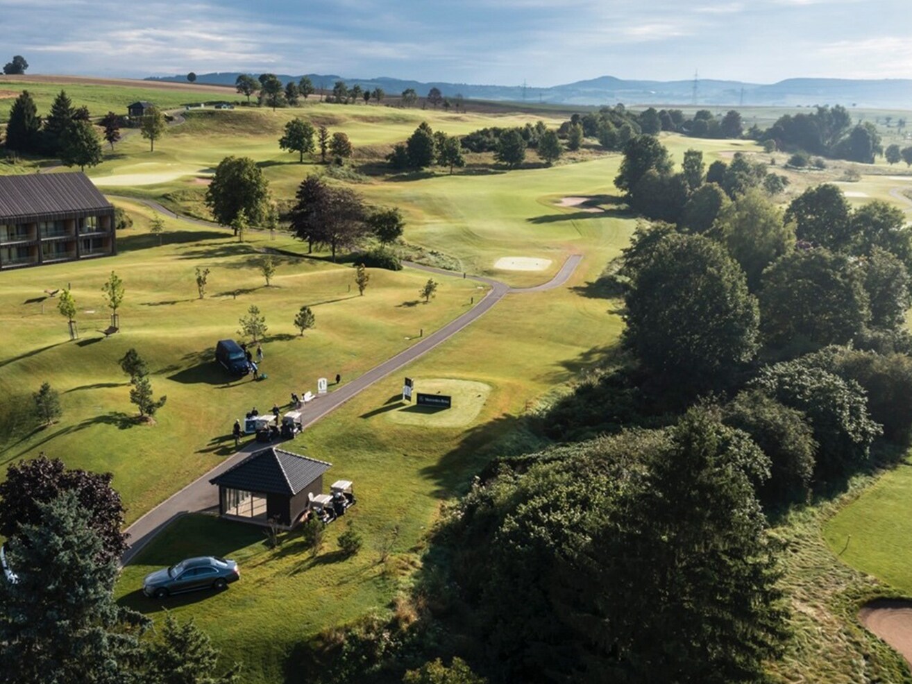 Golplatz aus der Vogelperspektive mit Bäumen und Autos.