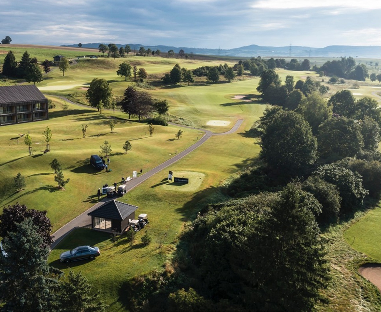Golf | Mercedes-Benz Golplatz aus der Vogelperspektive mit Bäumen und Autos.