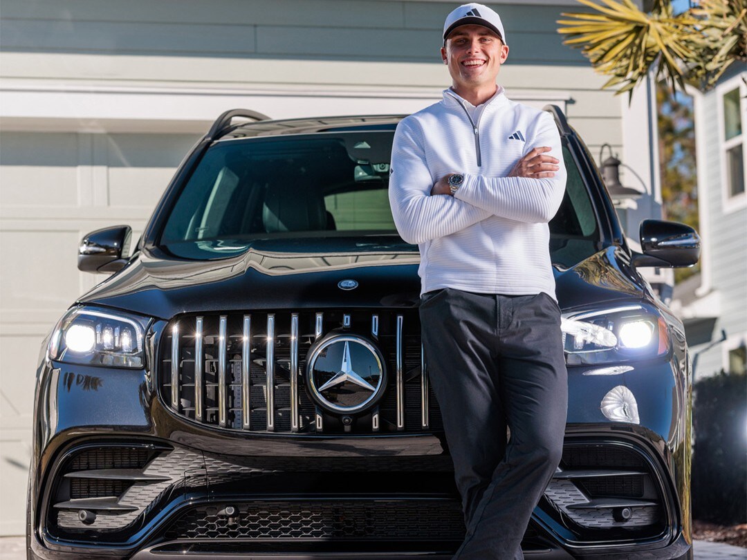 Ein Mann (Ludvig Aberg) lehnt an seinem Auto und lächelt.