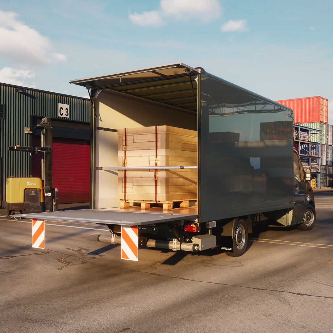 Mercedes‑Benz Sprinter mit Trockenfrachtkoffer‑Aufbau von Junge bei der Beladung im Logistikzentrum – effiziente Transportlösung für Stückgut und Warenverkehr. Die geöffnete Heckklappe zeigt palettierte Holzplatten im Laderaum während der Be‑ oder Entladung.