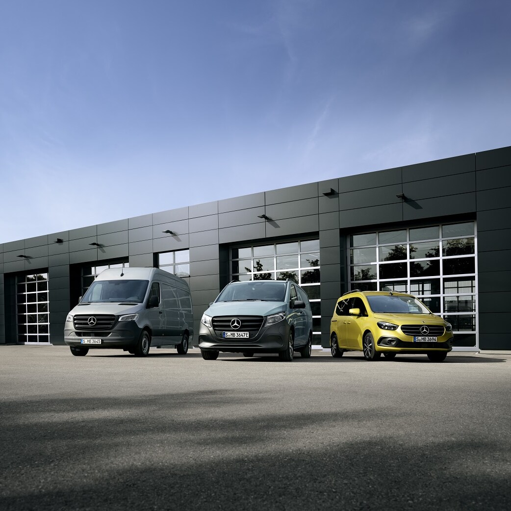 Mehrere Mercedes-Benz Transporter in einer Reihe vor modernem Gebäude, aufgenommen bei Tageslicht.