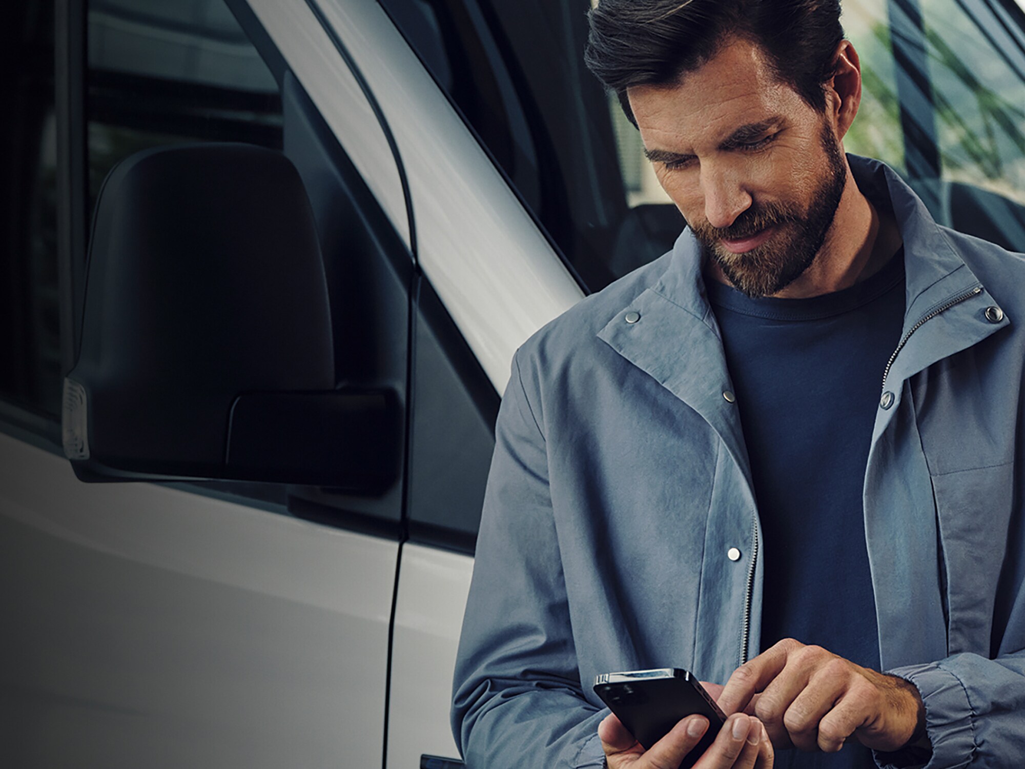 Ein Mann vor einem weißem Mercedes-Benz Transporter und tippt auf sein Mobiltelefon.