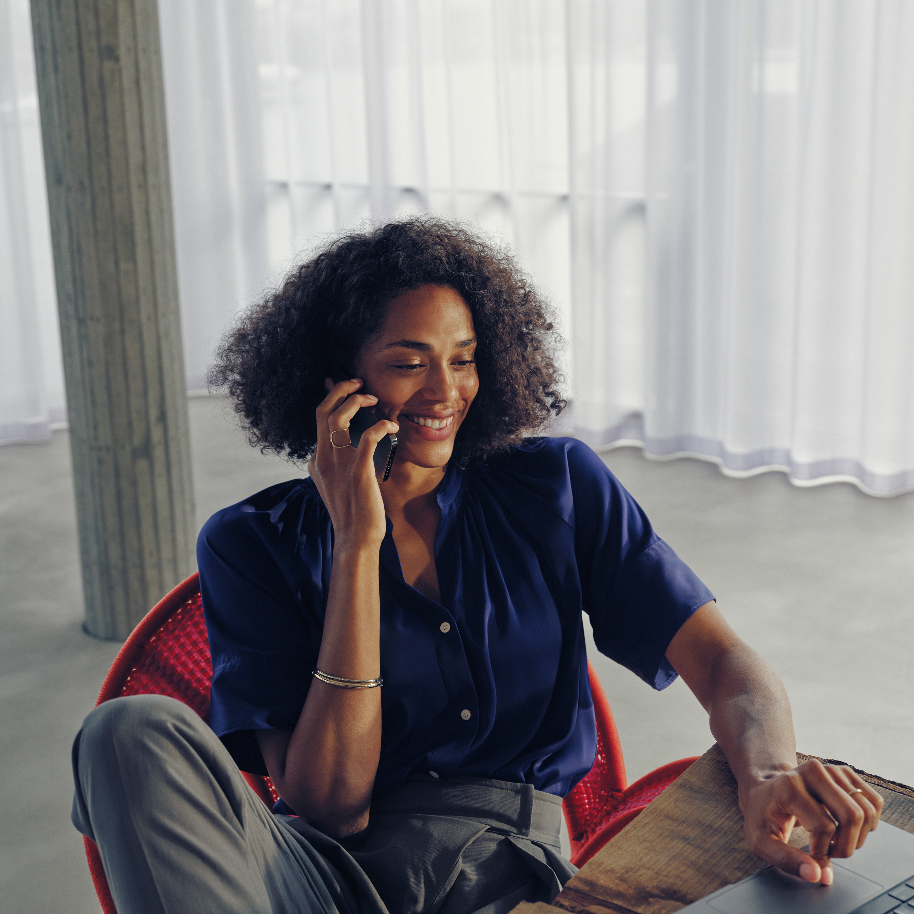 Neuwagen kaufen – So geht's | Mercedes-Benz Transporter. Eine Frau sitzt entspannt auf einem roten Stuhl und telefoniert breit lächelnd.