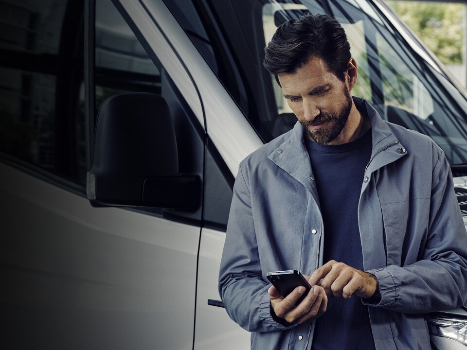 Ein Mann schaut auf sein Handy und stehtangelehnt an einen Mercedes-Benz Transporter.