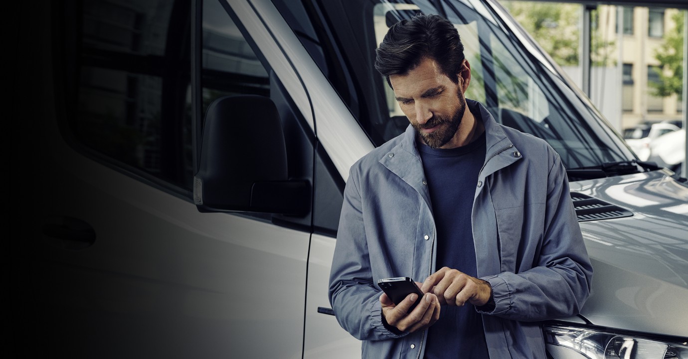 Neuwagen kaufen - so geht's! | Mercedes-Benz Ein Mann schaut auf sein Handy und stehtangelehnt an einen Mercedes-Benz Transporter.