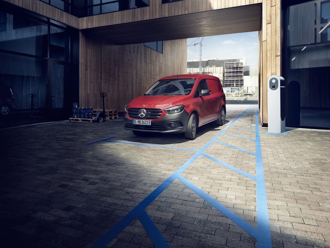 Ein roter Mercedes-Benz eCitan an einer Ladestation mit einer Baustelle im Hintergrund.