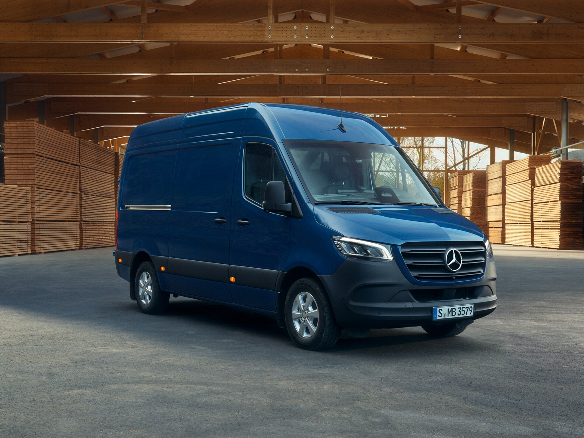 Ein blauer Mercedes-Benz Sprinter Kastenwagen, parkend vor Holzpaletten.