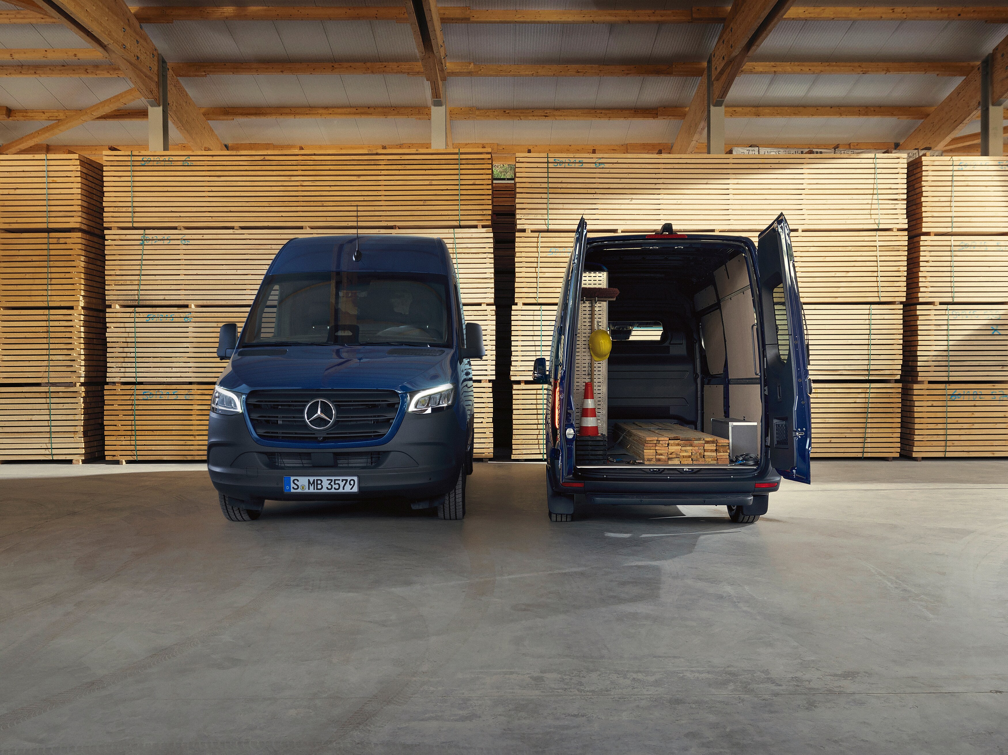 Ein blauer Mercedes-Benz Sprinter Kastenwagen, seitliche Ansicht, parkend vor Holzpaletten.