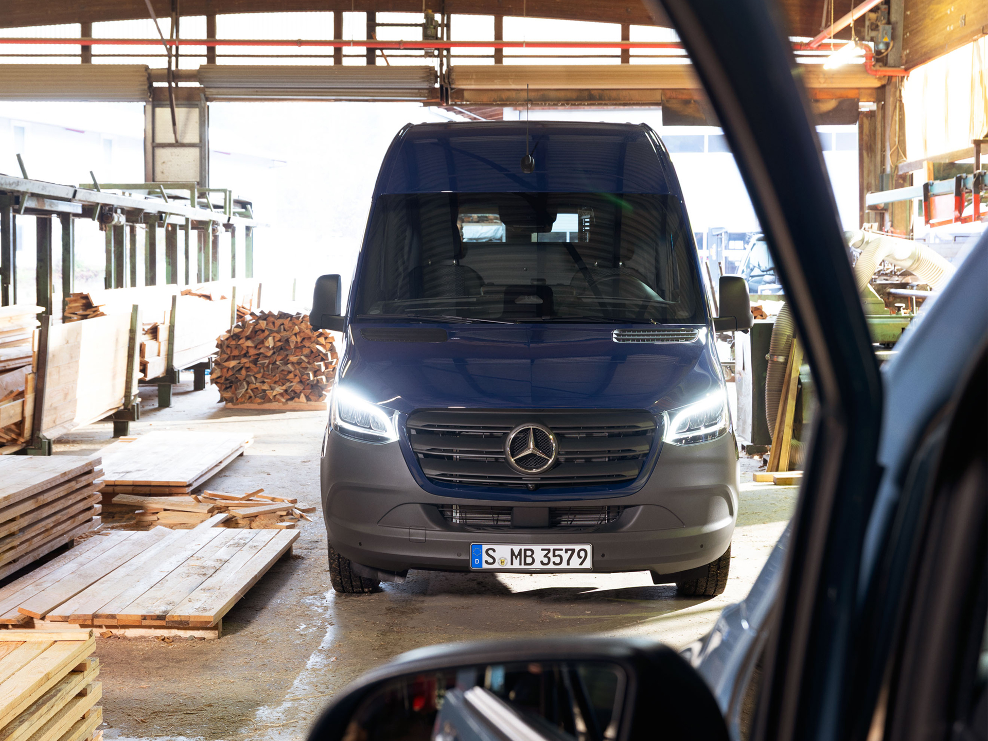Transporter Highlights | Mercedes-Benz Ein blauer Mercedes-Benz Sprinter Kastenwagen, parkend vor Holzpaletten.