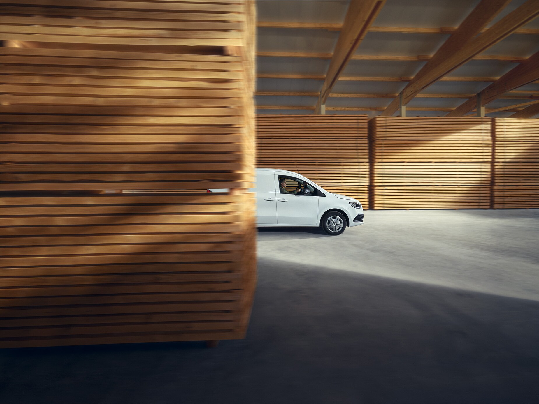 Ein weißer eCitan Kastenwagen, seitliche Ansicht, parkend vor Holzpaletten.