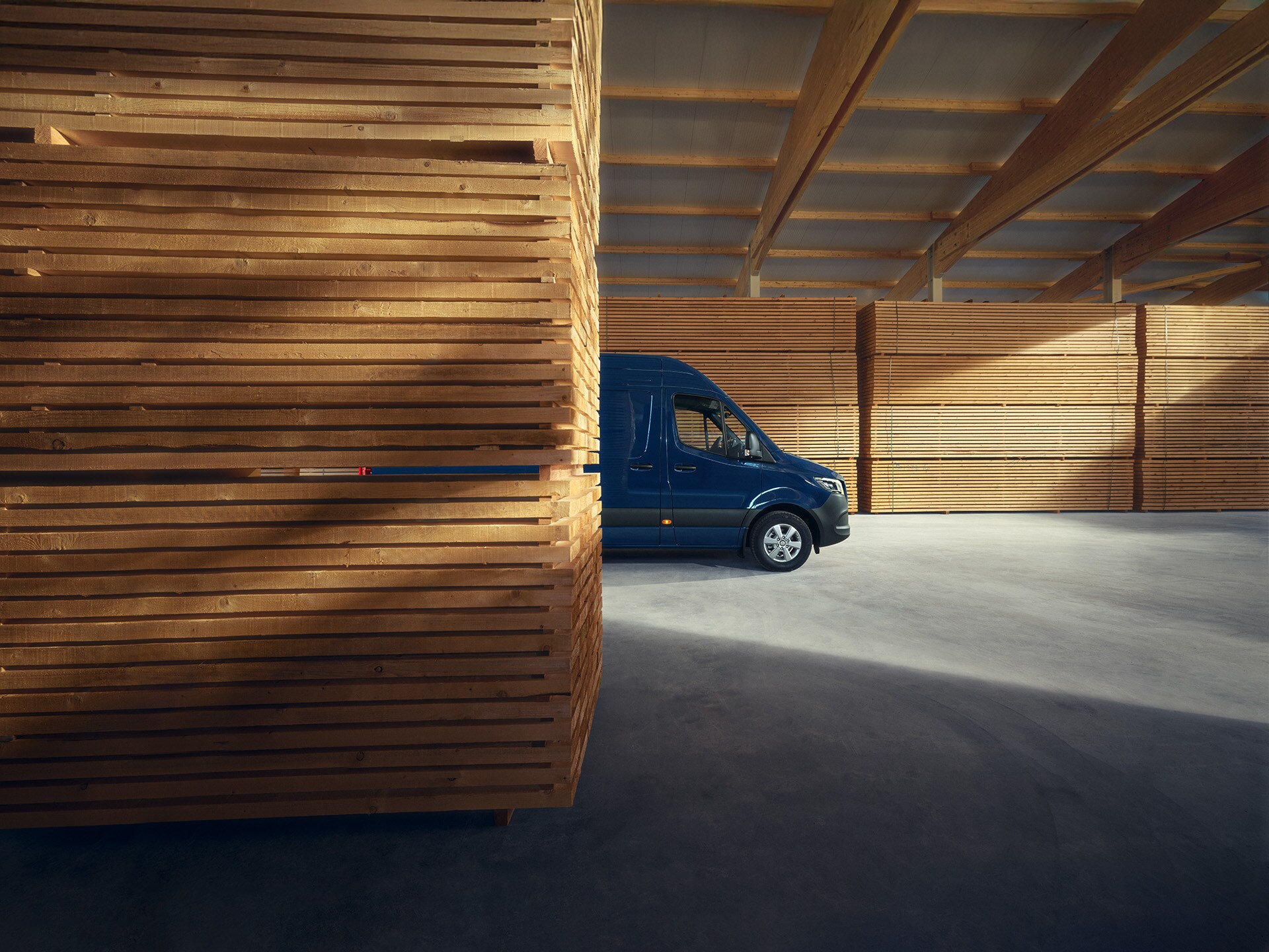 Ein blauer Mercedes-Benz Sprinter Kastenwagen, seitliche Ansicht, parkend vor Holzpaletten.