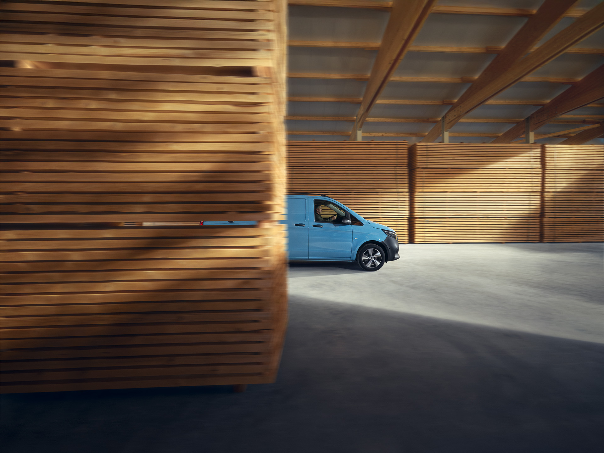 Transporter Highlights | Mercedes-Benz Ein hellblauer Mercedes-Benz eVito Kastenwagen, seitlicher Ansicht, parkend vor Holzpaletten.
