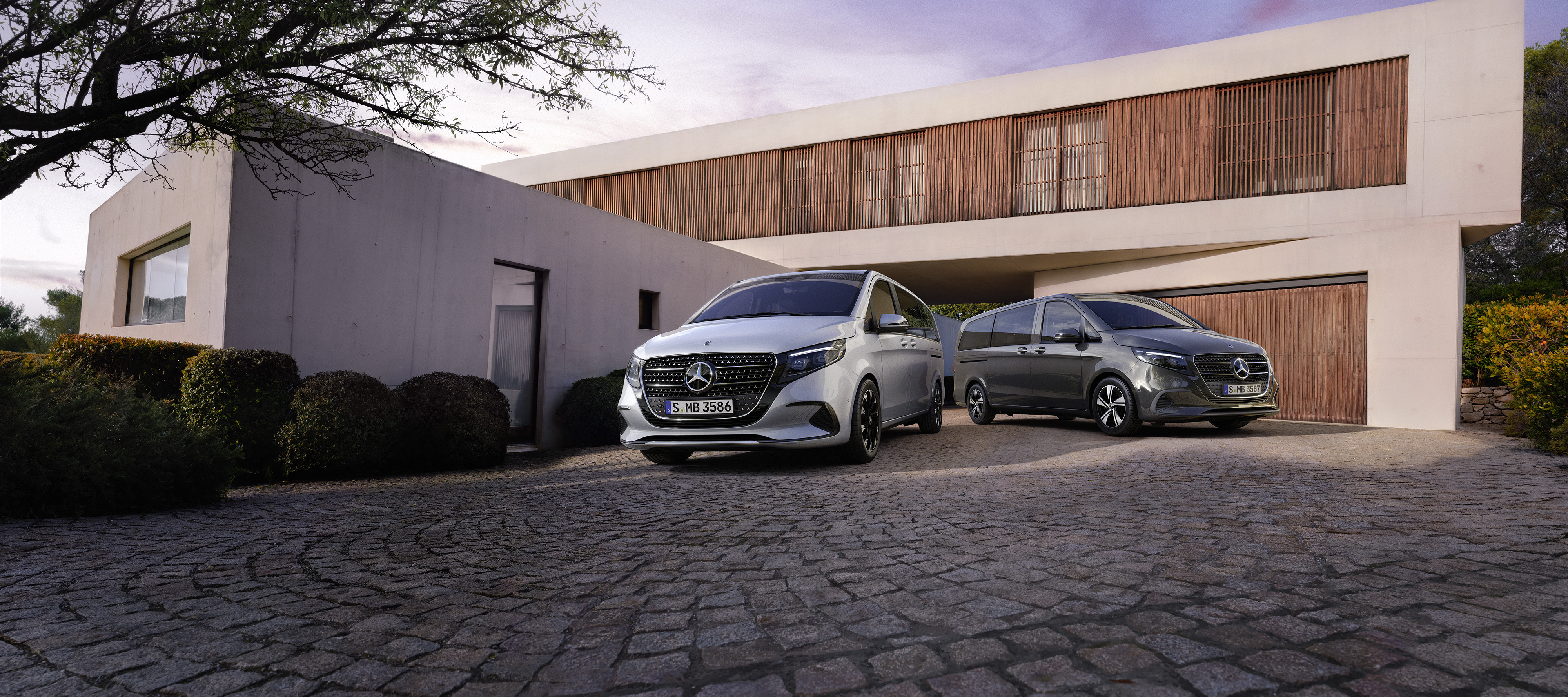 V-Klasse | Mercedes-Benz Zwei Mercedes-Benz V-Klassen parken vor einem mordernen Haus mit Garage.