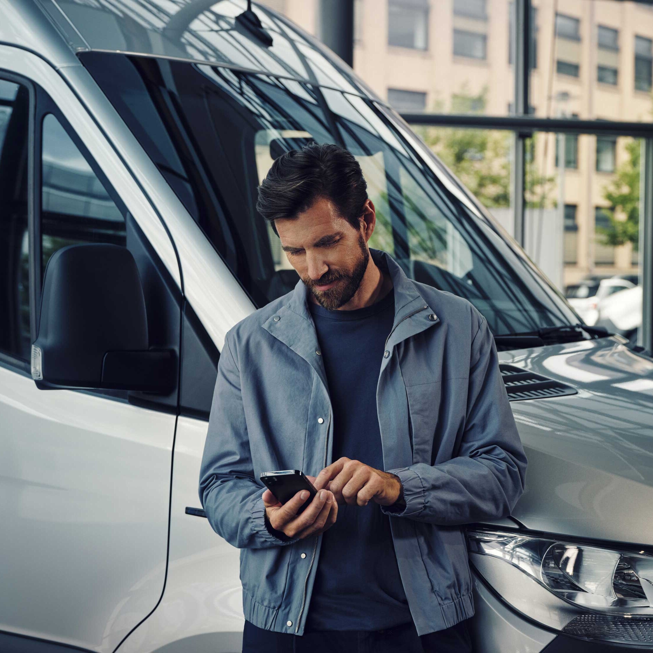 Eine Person steht vor einem Mercedes-Benz Transporter und tippt auf sein Handy.