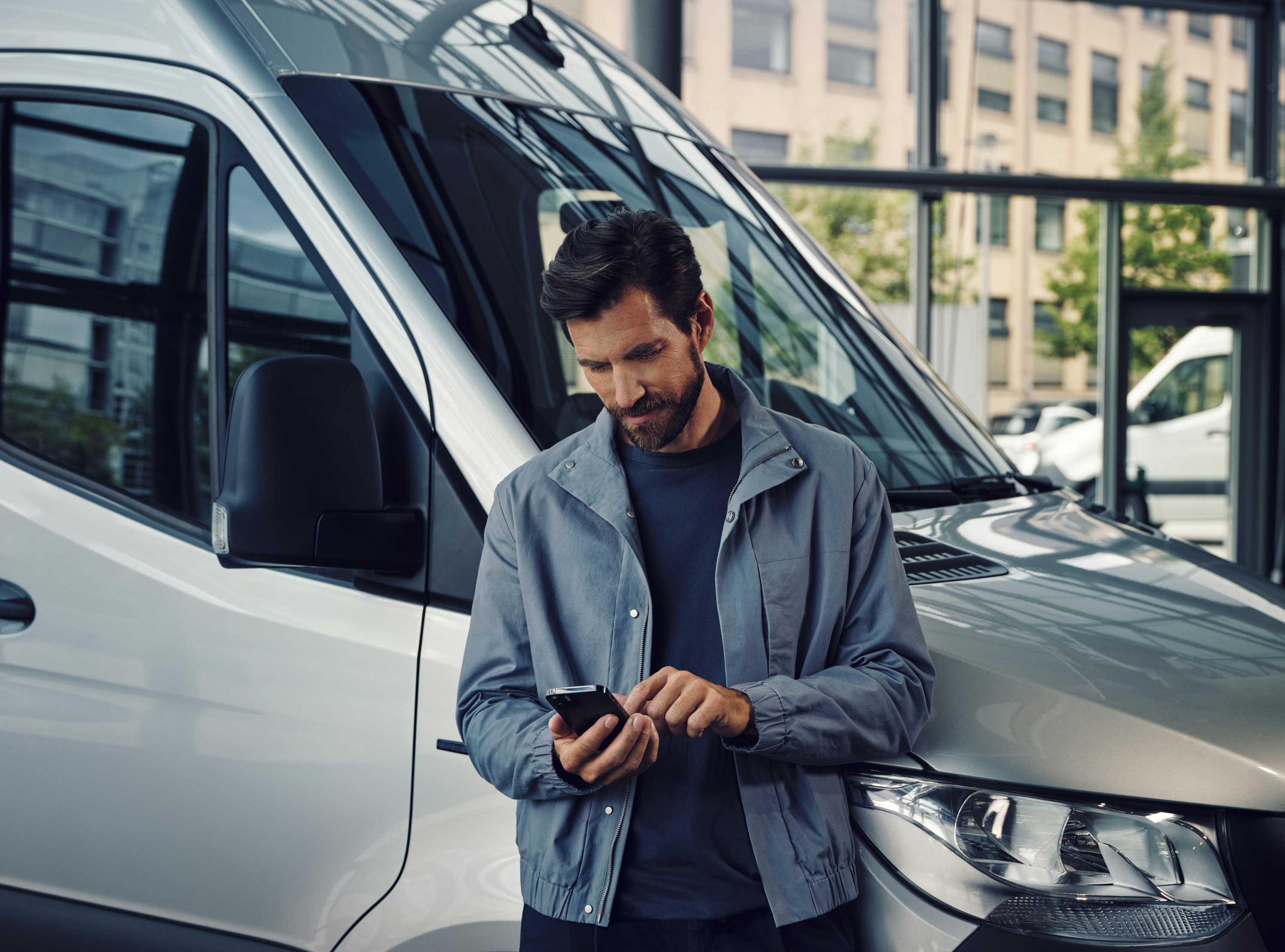Mercedes-Benz Kontakt Eine Person steht vor einem Mercedes-Benz Transporter und tippt auf sein Handy.