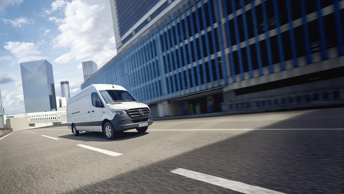 Ein weißer eSprinter Kastenwagen fährt auf einer Straße in einer urbanen Umgebung.
