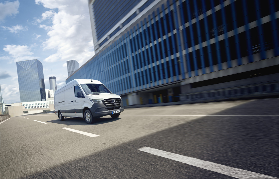 Ein weißer eSprinter Kastenwagen fährt auf einer Straße in einer urbanen Umgebung.