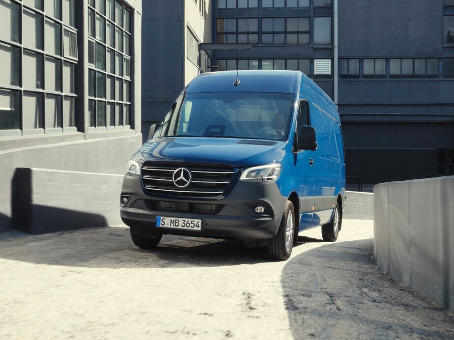 Ein blauer Sprinter Kastenwagen von Mercedes-Benz fährt um eine sanfte Kurve.
