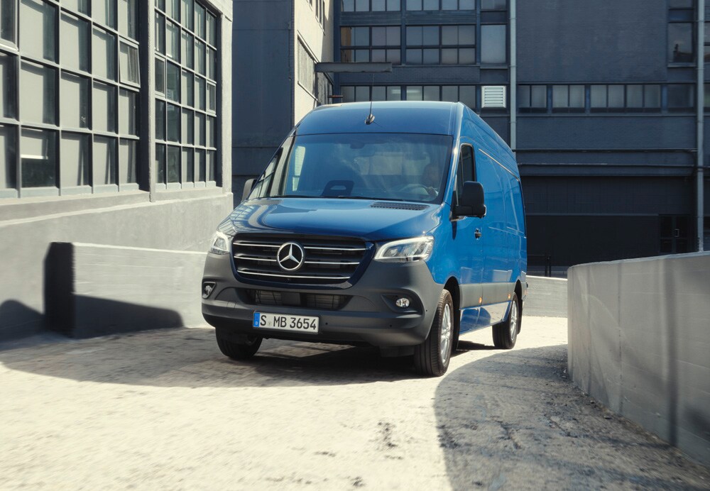 Leasingangebote | Mercedes-Benz Transporter. Ein blauer Sprinter Kastenwagen von Mercedes-Benz fährt um eine sanfte Kurve.