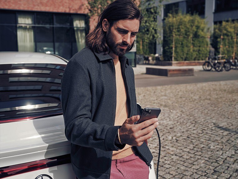 Mann geht neben einem schwarzen Mercedes-Benz EQV