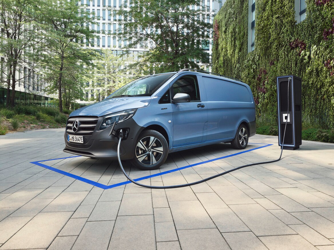 Ein hellblauer eVito Kastenwagen läft an einer Ladesäule im Hintergrund grüne Bäume stehend.