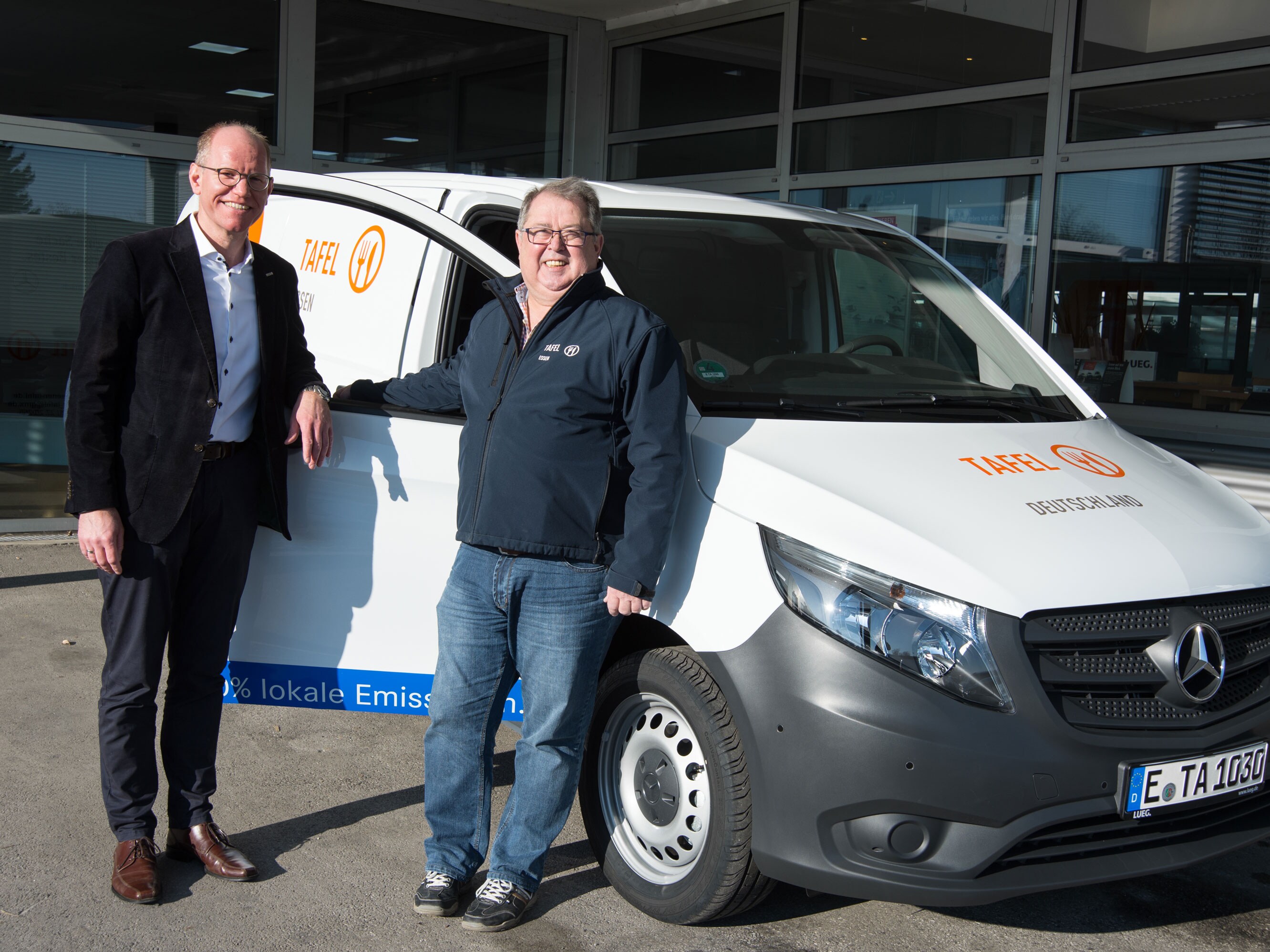 Zwei Personen lehnen sich an einen Mercedes-Benz Van und lächeln.