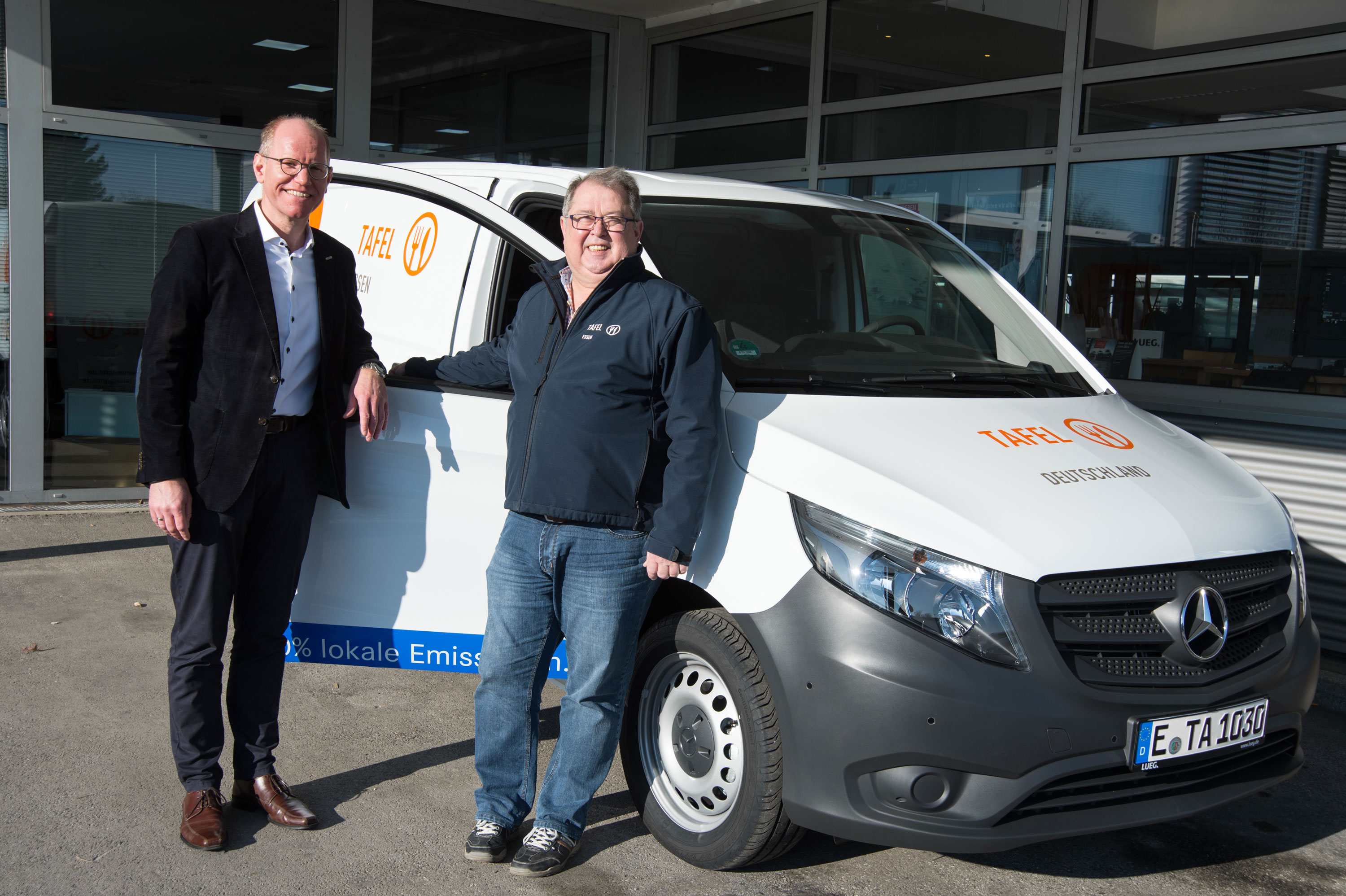 Mercedes-Benz | Tafel-Sponsoring Zwei Personen lehnen sich an einen Mercedes-Benz Van und lächeln.